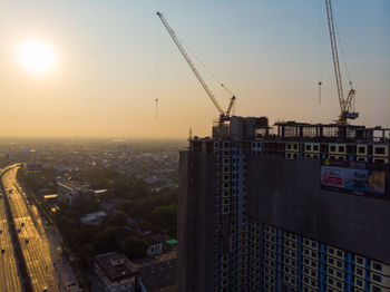 Construction site by buildings against sky during sunset