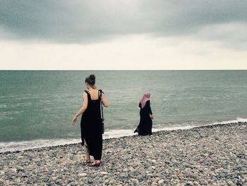 Rear view of couple standing at beach against sky