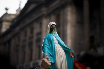 Close-up of hand holding statue against building