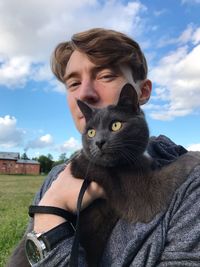 Portrait of young man with cat against sky