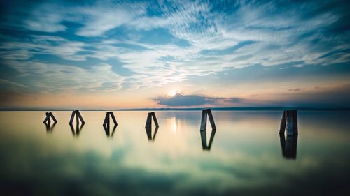 Wooden post in calm lake neusiedl against cloudy sky during sunset