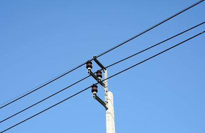 Low angle view of electricity pylon against clear blue sky