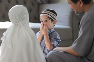 Side view of muslim father and kids greeting by touching their hands at home