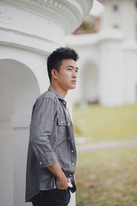 Young man looking away while standing by built structure