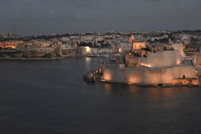 High angle view of illuminated cityscape by sea against sky