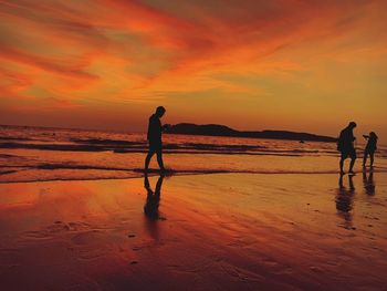 Silhouette people walking at beach against sky during sunset