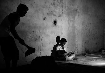 Man working with tool while boy reading book in darkroom