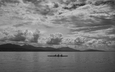 Silhouette men rowing on lake against cloudy sky