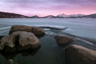 Rocks at shore against sky during sunset