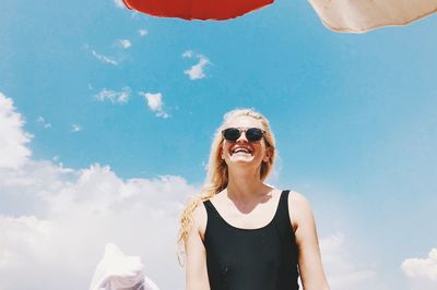 Low angle view of smiling woman wearing sunglasses against sky