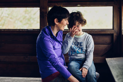 Happy mother and daughter sitting in log cabin