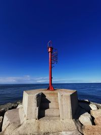 Lighthouse on rock by sea against blue sky