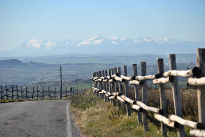 Fence on road by mountains against sky