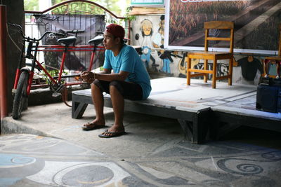 Full length of thoughtful mid adult man looking away while sitting on wood