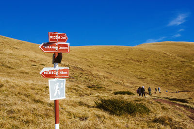 Directional sign on grassy field against mountains