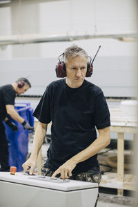 Male worker operating machine while coworker working in background