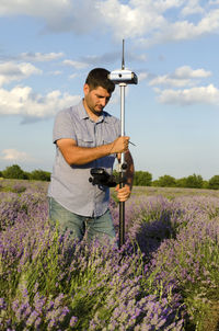 Surveyor with theodolite on lavender field against sky