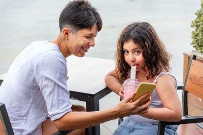 Mother and daughter drinking milkshake and looking at the mobile phone