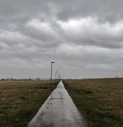 Road amidst field against storm clouds