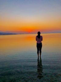 Rear view of woman standing at beach against sky during sunset
