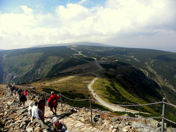 People on mountain road against cloudy sky