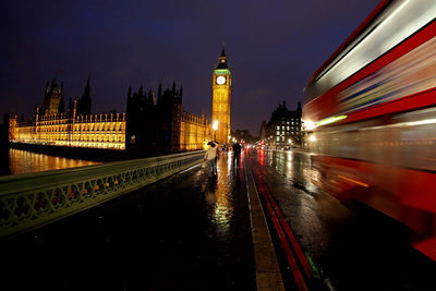 Red bus moving by big ben in city at night