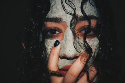 Close-up portrait of young woman with face paint against black background