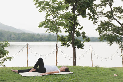 Pregnant young woman exercising while lying on mat over grass