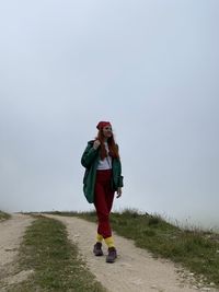 Full length of young woman standing against sky