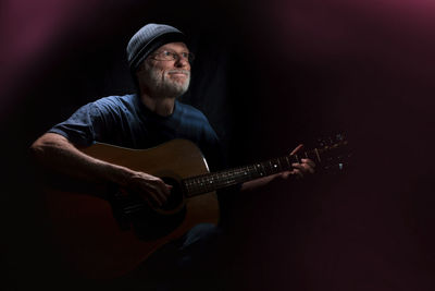 Smiling man playing guitar in darkroom