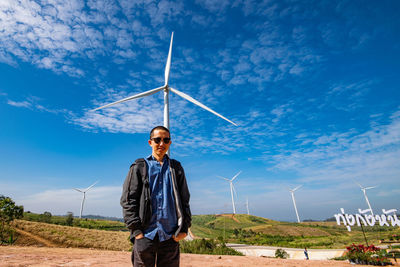 Man standing on land against wind turbine and sky