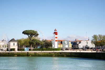 Lighthouse by buildings against clear blue sky