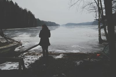 Rear view of woman standing by lake against sky