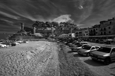 Cars parked at beach in town against cloudy sky