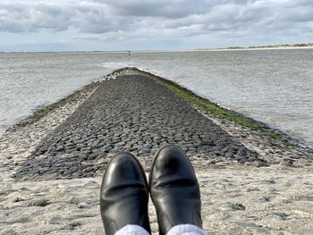 Low section of man on sea shore against sky