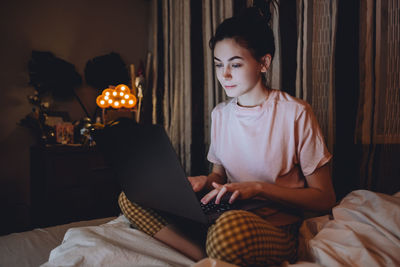 Young woman using laptop while sitting on bed at home