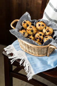 A basket of homemade blueberry muffins on a wooden chair.