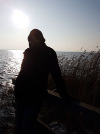 Rear view of silhouette man standing at beach against clear sky