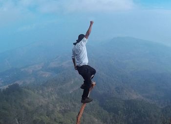 Full length of man on branch over mountain against sky