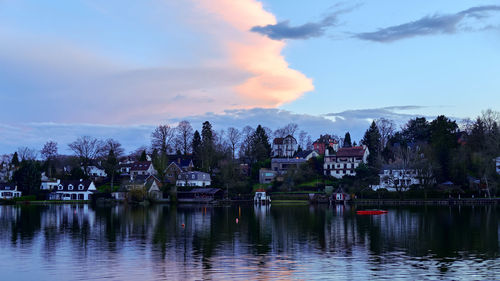 Scenic view of lake by buildings against sky at sunset