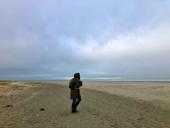 Rear view of woman walking at beach against sky