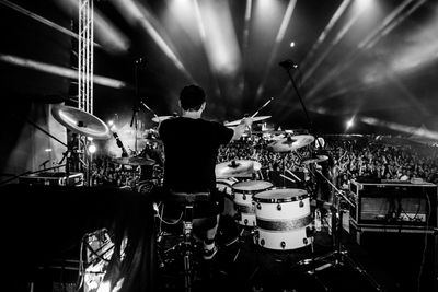 Rear view of drummer playing drums against crowd at music concert