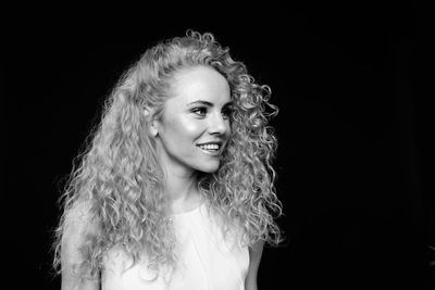Smiling woman with curly hair standing against black background