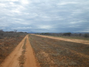 Road passing through field against cloudy sky