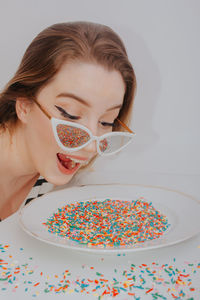 Close-up of woman wearing sunglasses with confetti against gray background