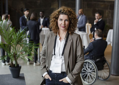 Portrait of confident businesswoman with hands in pockets standing at conference center during seminar