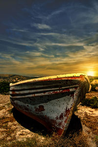Abandoned boat moored on beach against sky during sunset