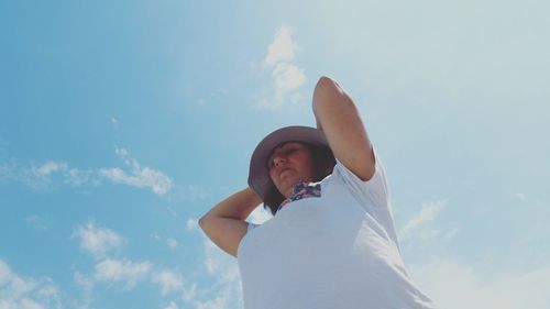 Low angle view of mature woman with arms raised standing against sky during sunny day
