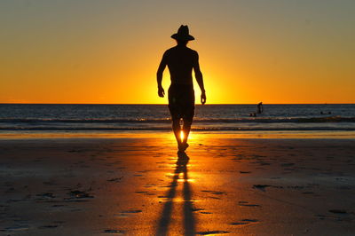 Rear view of silhouette man on beach against sky during sunset