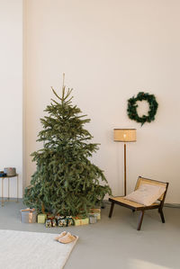 Christmas tree, a cozy armchair, a lamp and a wreath on the wall in a modern living room